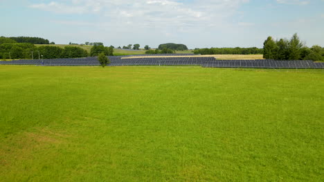 Aerial-Fly-Over-Solar-Farm-Built-in-the-Middle-of-a-Green-Grassy-Field-in-Zielenica,-Poland-on-Summer-Day,-Template-copy-space