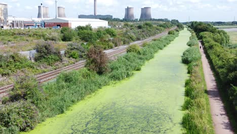 Green-algae-covered-canal-waterway-leading-to-power-station-industry-aerial-drone-view-slow-dolly-right