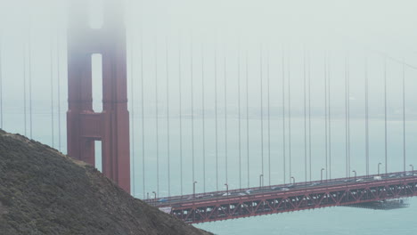 Eine-Mittlere-Aufnahme-Der-Golden-Gate-Bridge,-Während-Der-Verkehr-Am-Nebligen-Morgen-Hinüberfährt