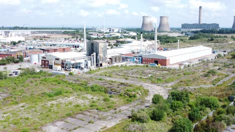 Industrial-warehouse-power-plant-refinery-buildings-under-smokestack-wasteland-aerial-view-zoom-in