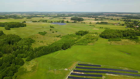Aerial-backwards-flight-over-large-solar-farm-complex-surrounded-by-green-landscape-in-nature