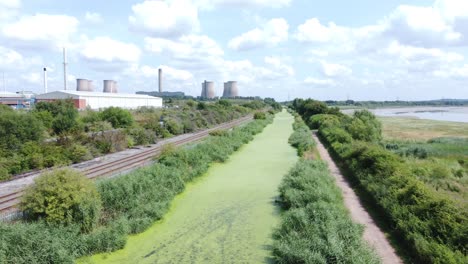 Green-algae-covered-canal-waterway-leading-to-power-station-industry-aerial-drone-view-pull-back-fast