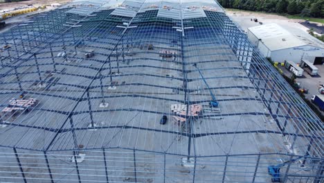 Construction-industry-metal-iron-girder-warehouse-framework-construction-site-aerial-view-tilt-down-drift