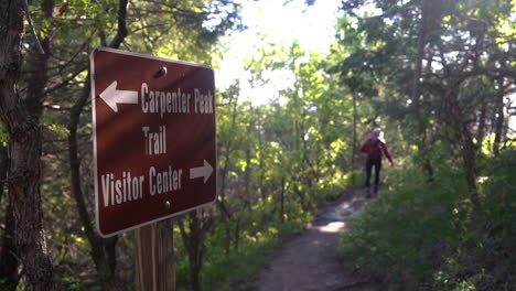 Roxborough-State-Park,-Colorado-Usa,-Carpenter-Peak-Und-Besucherzentrum-Schild-Mit-Wegbeschreibungen-Und-Weiblicher-Wanderer-Auf-Dem-Pfad-Im-Wald,-Vollbild-zeitlupe