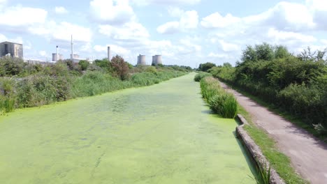 Green-algae-covered-canal-waterway-leading-to-power-station-industry-aerial-drone-view-low-forward-shot