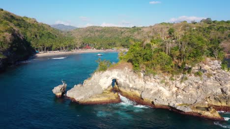Cinematic-aerial-video-of-Tropical-Island-with-turquoise-water-waves-crushing-rocky-cliffs,-arch,-boats,-coastline,-Crystal-Bay-Beach,-nusa-penida,-bali,-Indonesia,-Aerial-view