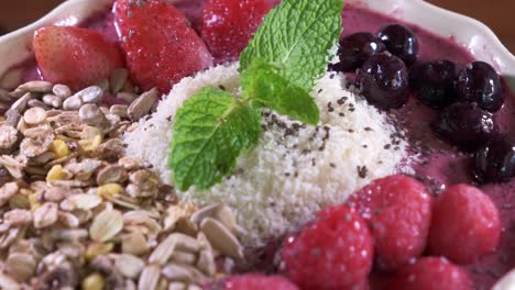 smoothie-bowl-with-Strawberries,-Oats,-Grains-and-Blueberries-in-a-White-Bowl-Close-Up-Spinning-on-Table
