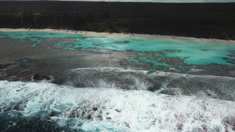 Aerial-shot-of-waves-breaking-over-reef-on-secluded-Yejele-Beach,-New-Caledonia