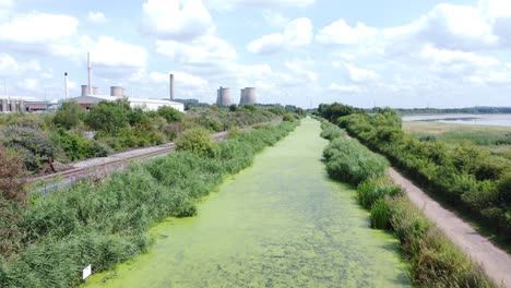 Green-algae-covered-canal-waterway-leading-to-power-station-industry-aerial-drone-view