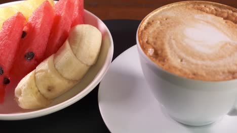 A-Hot-Cup-of-Coffee-with-Foam-and-a-Dish-of-Side-Fruit-Spinning-on-a-Plate