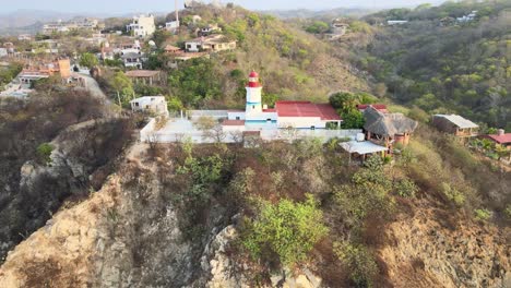 Pull-back-from-small-lighthouse-to-sea,-until-to-panoramic-view-with-ocean,-cliff-and-mountains-at-the-same-time,-in-Oaxaca's-shore,-Mexico