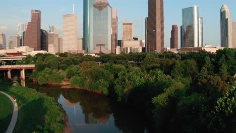 Houston-Texas-Skyline-Buffalo-Bayou-Park-aerial-rise-up-above-river-towards-skyscrapers-4k-drone
