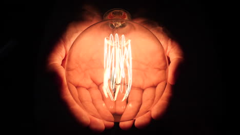 Caucasian-hands-holding-large-light-bulb,-flashing-on-and-off