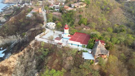Orbital-view-of-small-lighthouse-above-cliff-at-afternoon,-in-Oaxaca's-shore