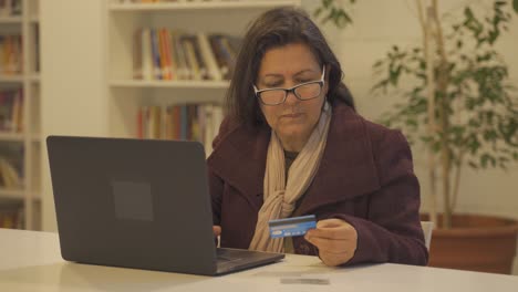 Old-woman-sitting-on-table-with-laptop-and-buying-products-online-with-credit-card