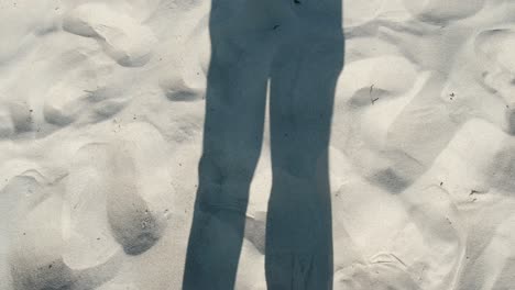 Schatten-Der-Beine-In-Hosen,-Die-Im-Wind-Auf-Sandigem-Hintergrund-Wehen