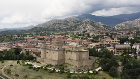 Sweeping-aerial-flypast-over-the-New-Castle-of-Manzanares-and-surrounding-town-to-reveal-the-Sierra-de-Guadarrama-dramatic-mountain-ranges-on-the-horizon