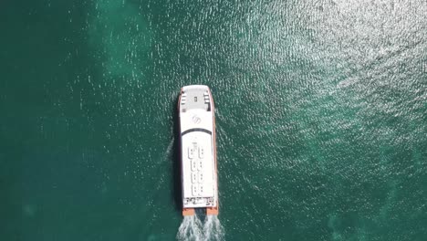 Aerial-drone-tracking-video-of-ferry-Utila-dream-in-deep-blue-open-Caribbean-sea,-arriving-to-the-island-of-Utila,-Honduras