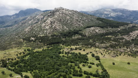 Pan-down-aerial-view-over-the-mountain-ranges-of-Sierra-De-Guadarrama-and-the-surrounding-foothills-of-Manzanares-el-Real,-Community-of-Madrid-in-Spain