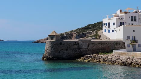 Schöne-Statische-Ansicht-Eines-Alten-Turms-Mit-Weißen-Häusern-Nahe-Der-Wasserseite-In-Ibiza,-Mediterraner-Feiertagshintergrund