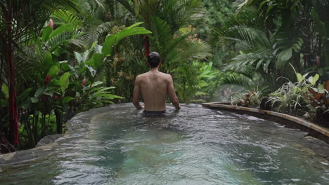 Man-in-lavish-infinity-pool-in-rain-forest-looking-out-at-surroundings