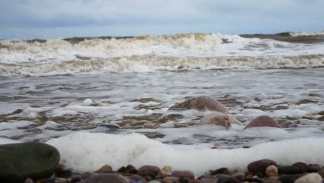 Foamy-breaking-ocean-surf-pebble-beach-shoreline-tide-soothing-multicoloured-stones-closeup-left-dolly