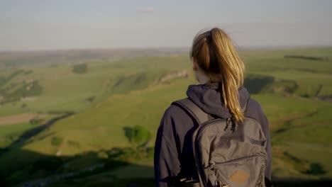 Handheld-rotating-shot-of-young-blonde-woman-admiring-the-view-from-the-top-of-Mam-Tor,-Castleton,-Peak-District,-England-at-sunset