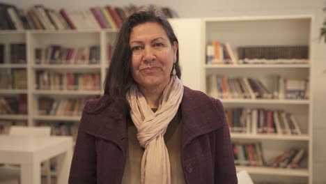 Pretty-middle-aged-woman-smiling-at-camera-standing-inside-library,close-up-shot