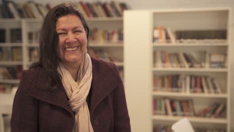 Middle-aged-woman-in-library-room-laughs-while-looking-at-camera