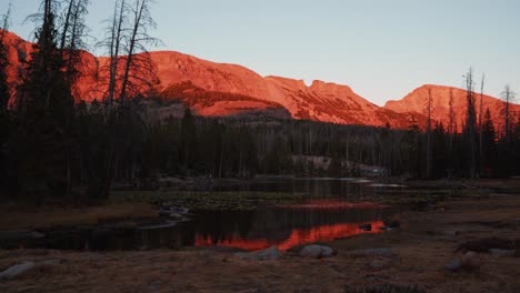 Stunning-time-lapse-landscape-shot-of-the-beautiful-Butterfly-Lake-surrounded-by-large-rocky-mountains-and-pine-trees-inside-of-the-Uinta-Wasatch-Cache-National-Forest-in-Utah-during-a-summer-sunset