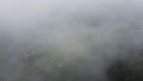Aerial-mountain-village-below-clouds-in-moody-atmosphere-4K