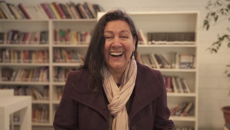 Beautiful-Middle-aged-woman-laughing-in-library-out-loud-looking-at-camera-stand-indoors