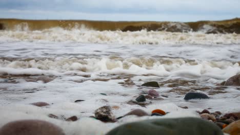 Foamy-breaking-ocean-surf-pebble-beach-shoreline-tide-soothing-multicoloured-stones-left-dolly