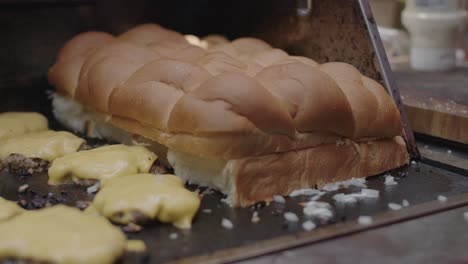 Chef-places-dinner-roll-bread-onto-the-hot-grill-with-chopped-onion