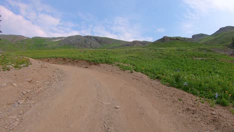 POV-driving-on-Black-Bear-Pass-trail-cut-into-hillside-through-alpine-valley-with-waterfall-in-distance-near-Telluride-Colorado