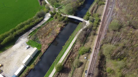 Green-and-brown-tree-and-blue-canal,-aerial-view-of-train-track-and-bridge-in-the-north-of-the-UK