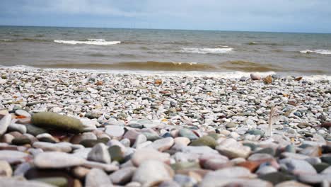 Foamy-breaking-ocean-surf-pebble-beach-shoreline-tide-soothing-multicoloured-stones-closeup-right-dolly-shot