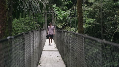 Tourist-walks-over-hanging-bridge-in-tropical-rain-forest-camera-in-hand