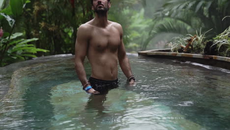 Man-looks-up-at-tree-tops-while-in-luxury-pool-in-rain-forest,-slow-motion