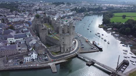 Ancient-Caernarfon-castle-Welsh-harbour-town-aerial-view-medieval-waterfront-landmark-quick-zoom-out