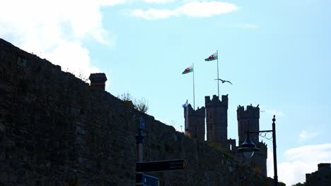 Torre-Del-Castillo-De-Caernarfon-Postes-De-Bandera-Que-Sostienen-Emblemas-De-Dragones-Galeses-De-Gales-Que-Soplan-En-La-Brisa-Costera