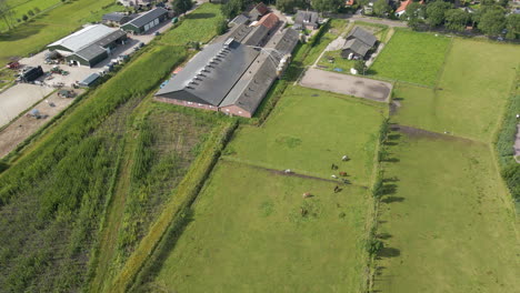 Aerial-of-large-farm,-tilting-up-and-revealing-rural-town-in-the-distance