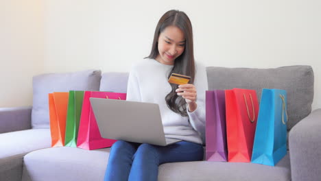 Asian-shopaholic,-beautiful-exotic-woman-shopping-online-using-laptop-and-credit-card,-slow-motion-full-frame