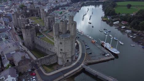 Ancient-Caernarfon-castle-Welsh-harbour-town-aerial-view-medieval-waterfront-landmark-slow-left-overlooking-dolly