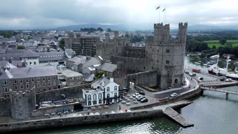 Ancient-Caernarfon-castle-Welsh-harbour-town-aerial-view-medieval-waterfront-landmark-slow-right-over-river