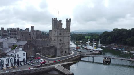 Ancient-Caernarfon-castle-Welsh-harbour-town-aerial-view-medieval-waterfront-landmark-fast-dolly-left-low-angle