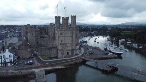 Ancient-Caernarfon-castle-Welsh-harbour-town-aerial-view-medieval-waterfront-landmark-close-left-dolly