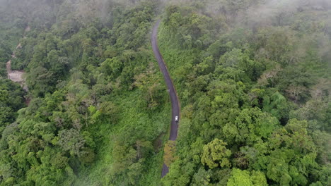 Aerial-moving-through-clouds-overhead-following-car-along-windy-jungle-road,-4K