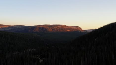 Dolly-out-landscape-aerial-shot-of-a-canyon-in-the-Uinta-Wasatch-Cache-National-Forest-in-Utah-with-a-highway-below-surrounded-by-pine-trees-and-rocky-mountains-during-a-vivid-summer-sunset