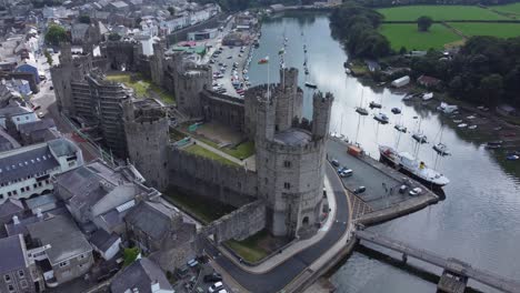 Ancient-Caernarfon-castle-Welsh-harbour-town-aerial-view-medieval-waterfront-landmark-rising-birdseye-shot